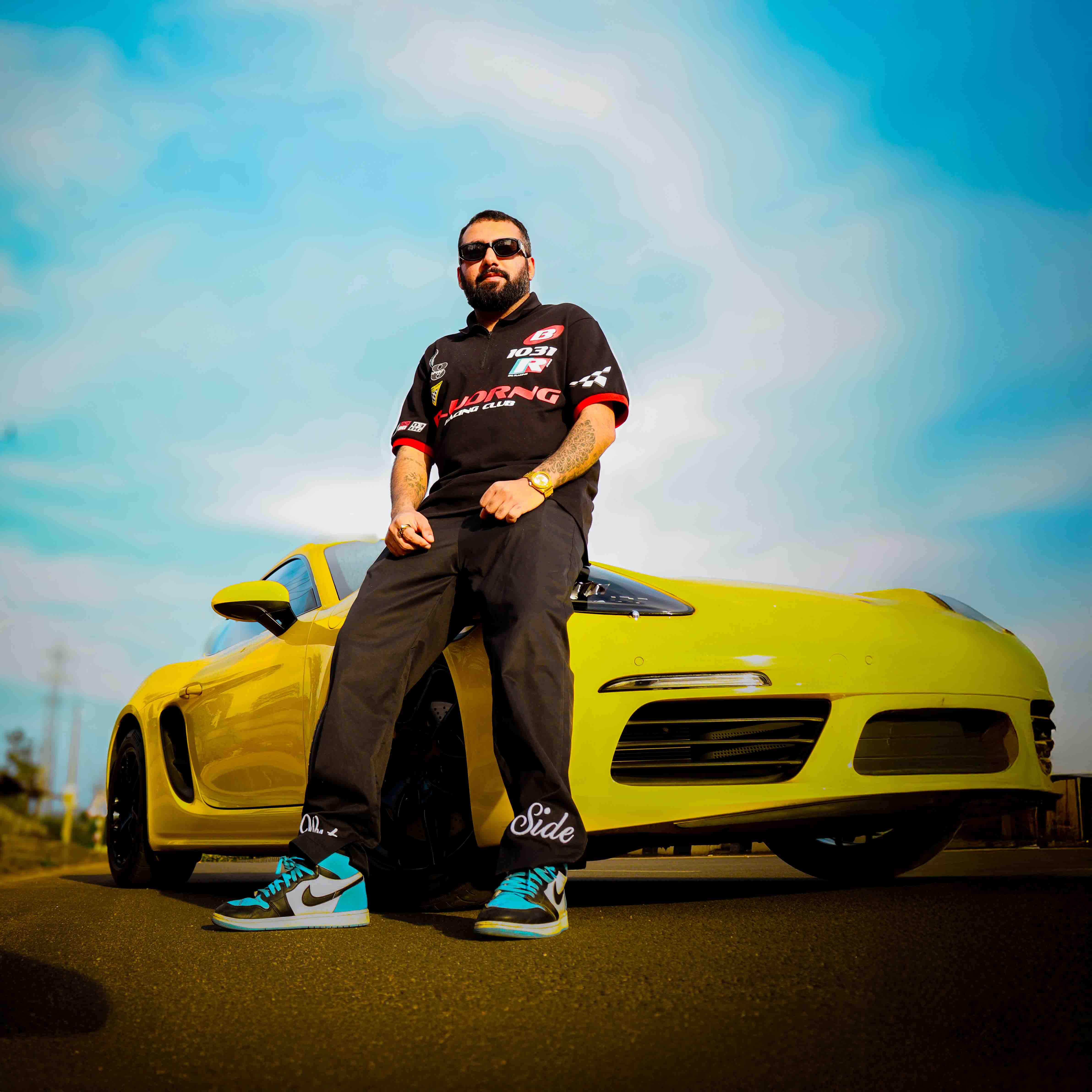 Man posing confidently by a yellow Porsche 718 Cayman during a professional photoshoot
